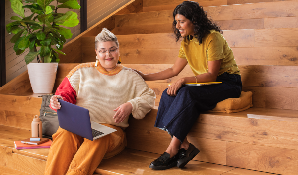 Two women sitting on large wooden steps, working out their small business marketing strategy together.