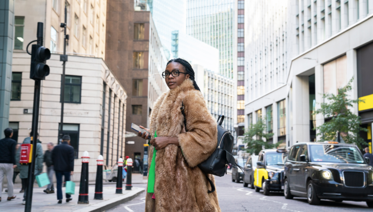 A stylish woman in a fur coat and green shirt confidently crossing a London street