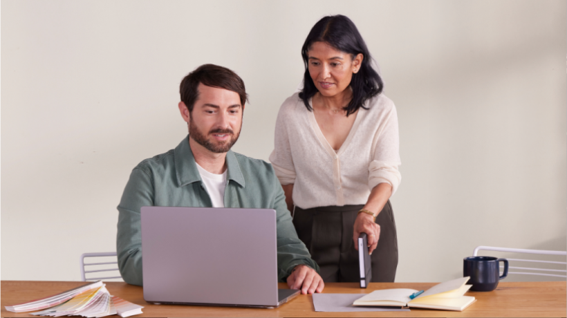 A man and woman looking at a laptop together while discussing AI marketing strategy.