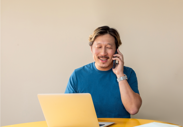 A man in front of his laptop, getting help from a friendly Mailchimp customer service agent by phone.