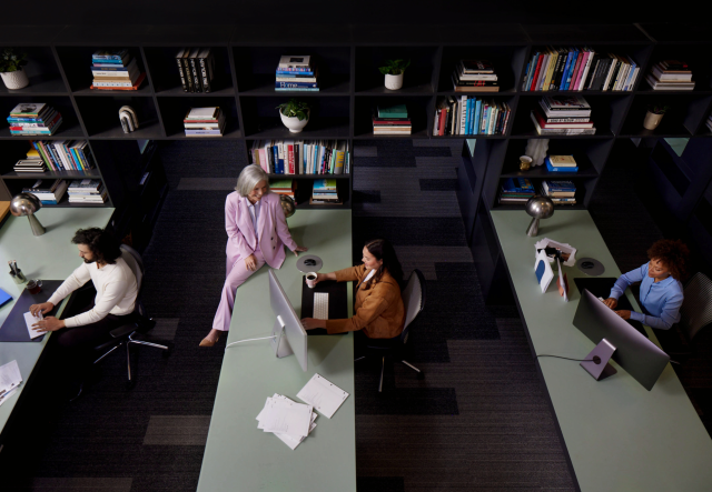 A birds-eye-view of an office, containing coworkers at their desks, working and chatting.