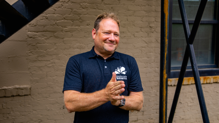 Co-founder of Freshtix, Iain Bluett smiles while sporting a branded t-shirt outside of the Freshtix office.